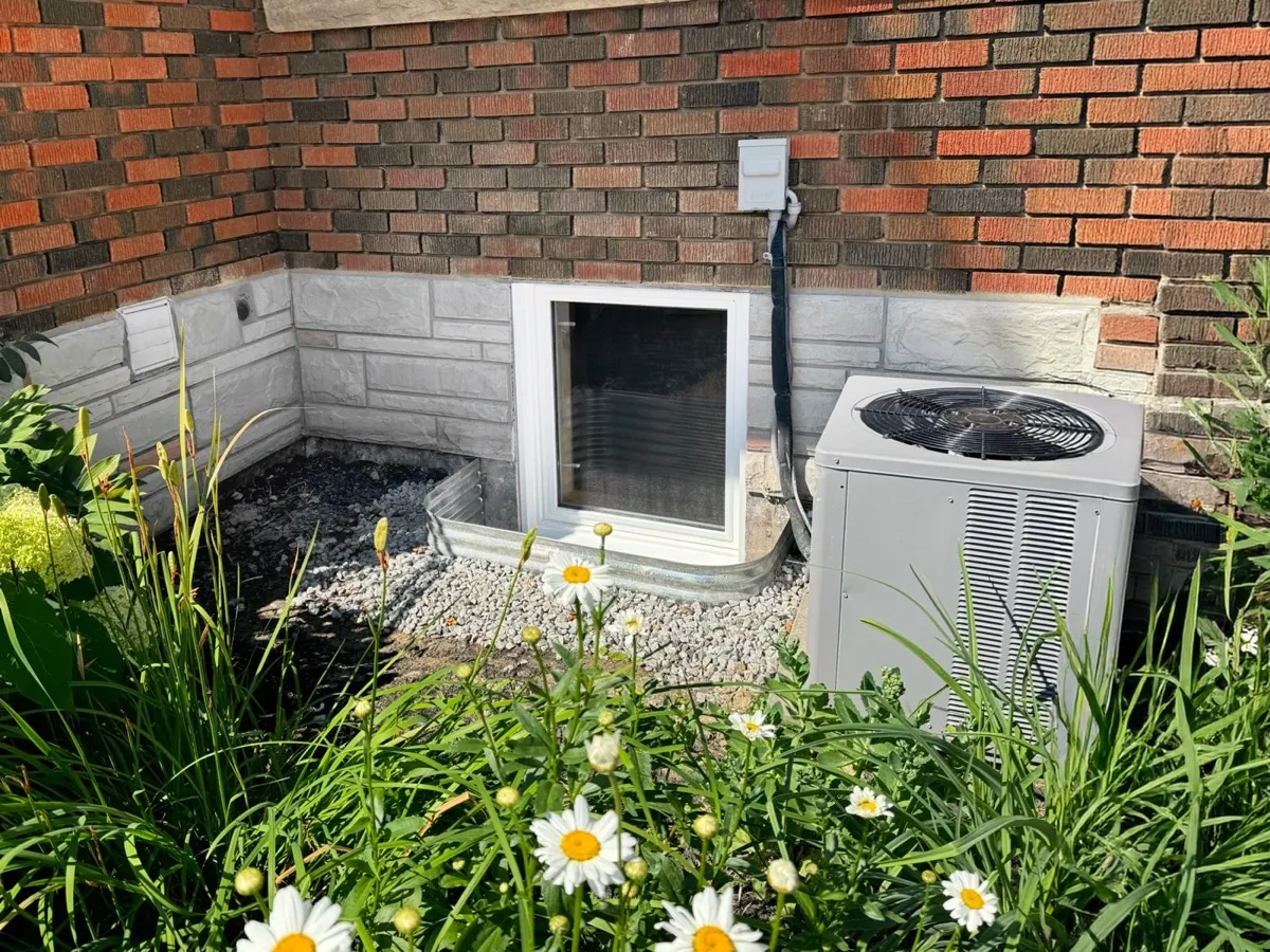 Finished basement egress window in a well with drainage stone beside a garden