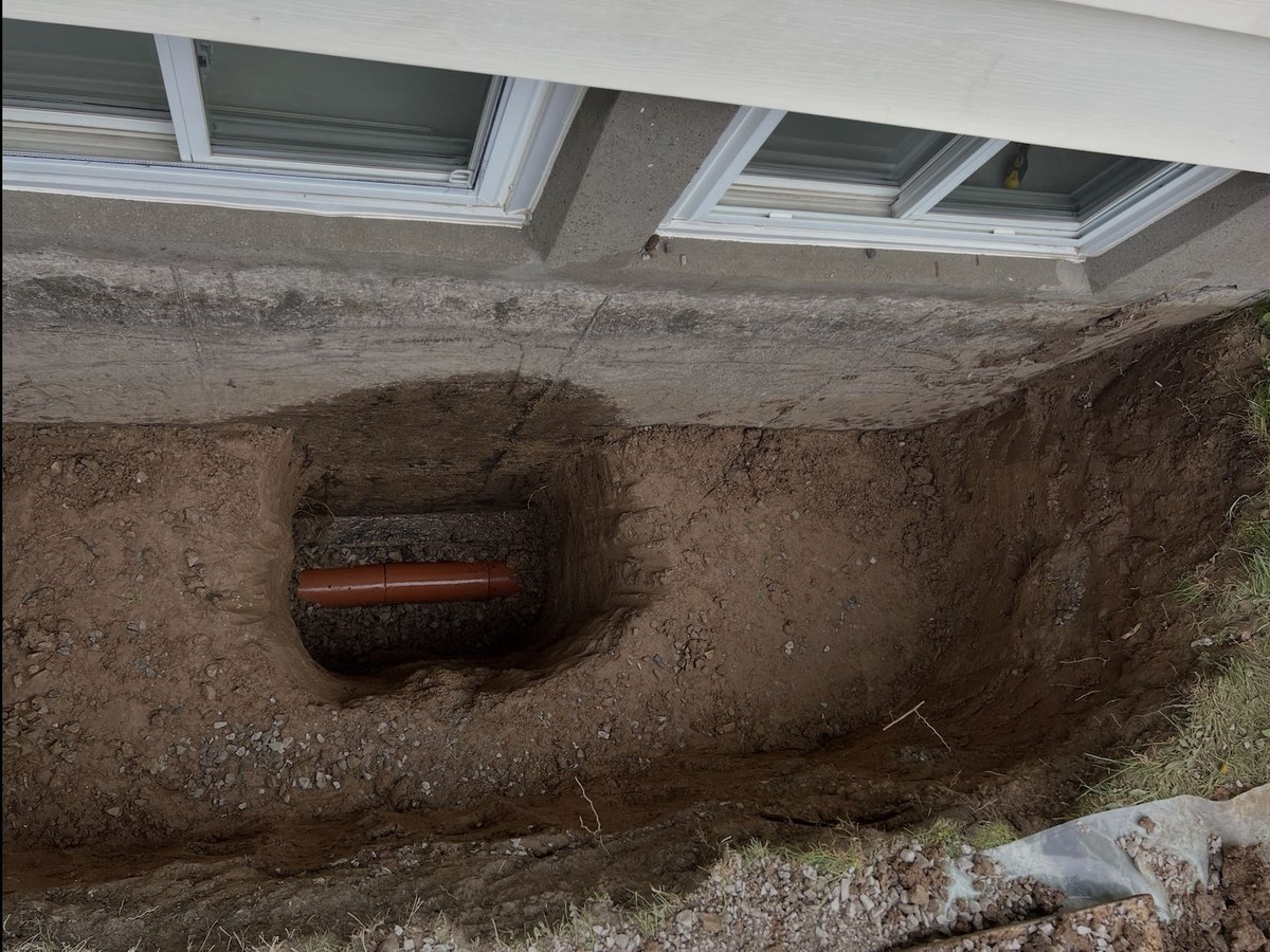 Hand dug window well excavation with the clay weeping tile exposed below the basement windows