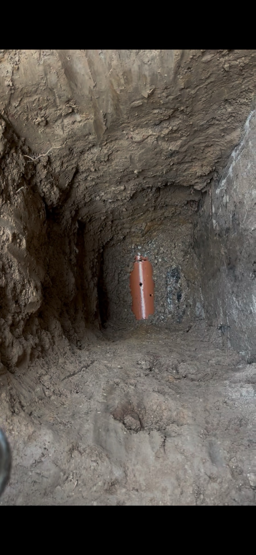 Shiny clay weeping tile at the end of a hand dug window well shaft