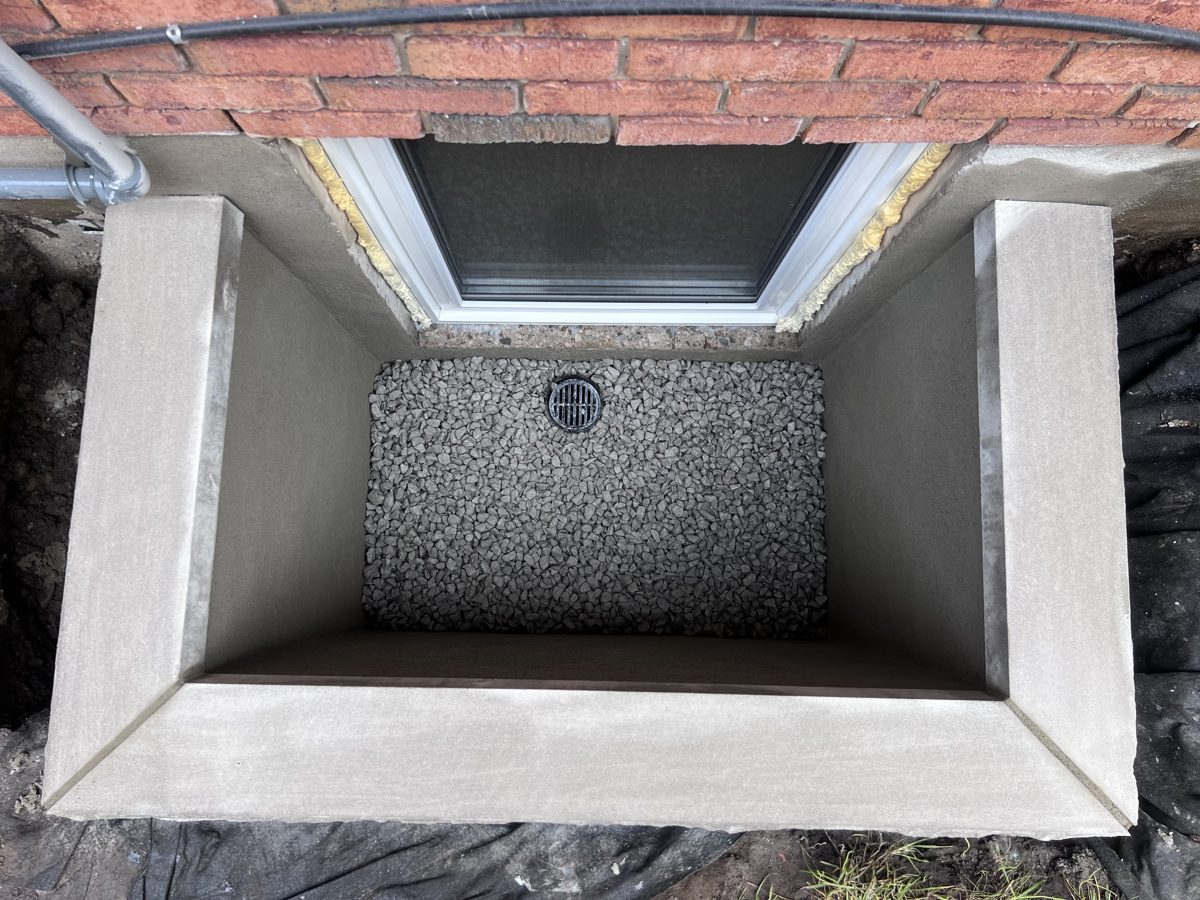 Custom masonry window well during the build, parged walls with the drain set in the stone bed