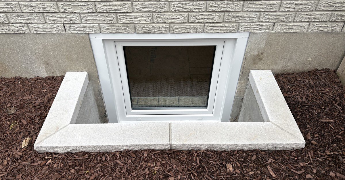 Finished window well with a limestone sill at grade beside fresh mulch