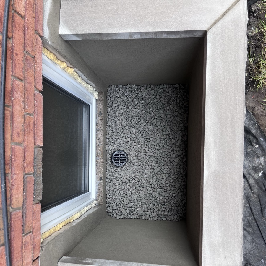 Overhead view of a finished masonry window well with parged walls, drainage stone, and floor drain