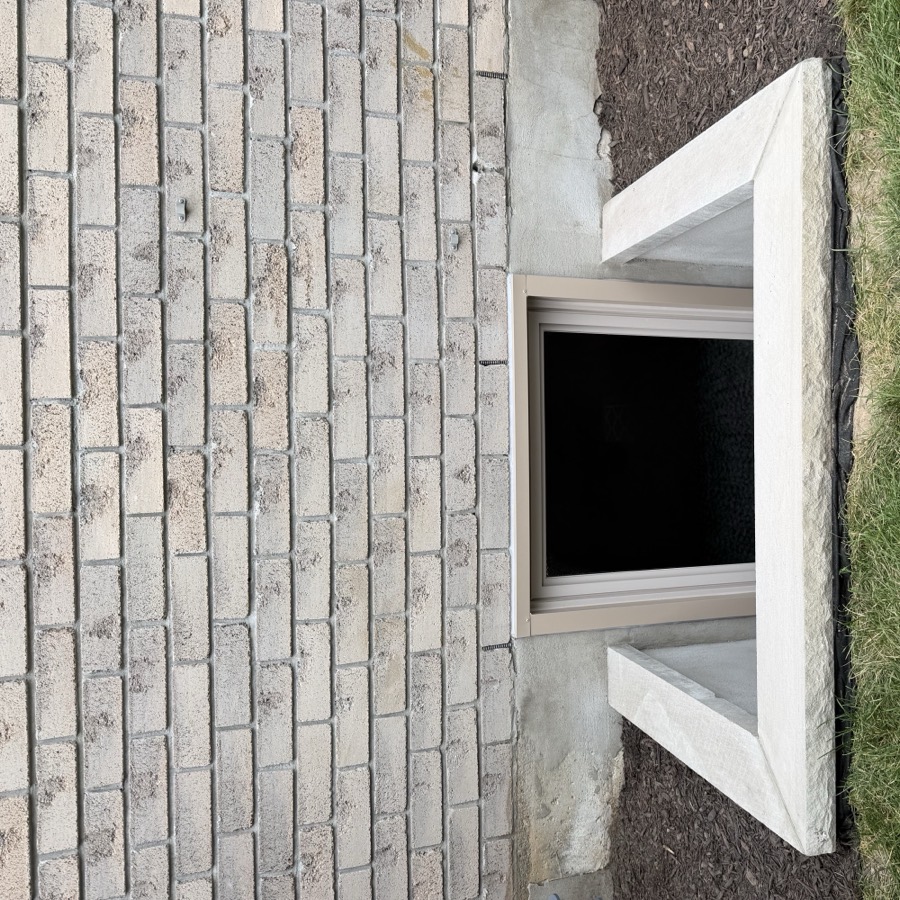 Masonry window well with a rock face limestone sill against a sand brick wall